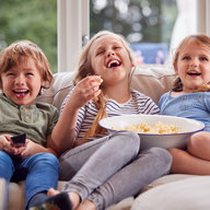 Drei Kinder sitzen vorm Fernseher und essen Popcorn