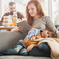Frau liest Buch während Kind auf ihrem Schoß schläft