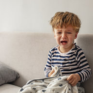 kleiner blonder Bub sitzt am Sofa und schreit vor Wut