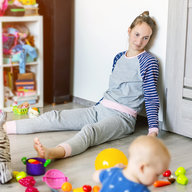 Frau lehnt fix und fertig an Zimmerwand