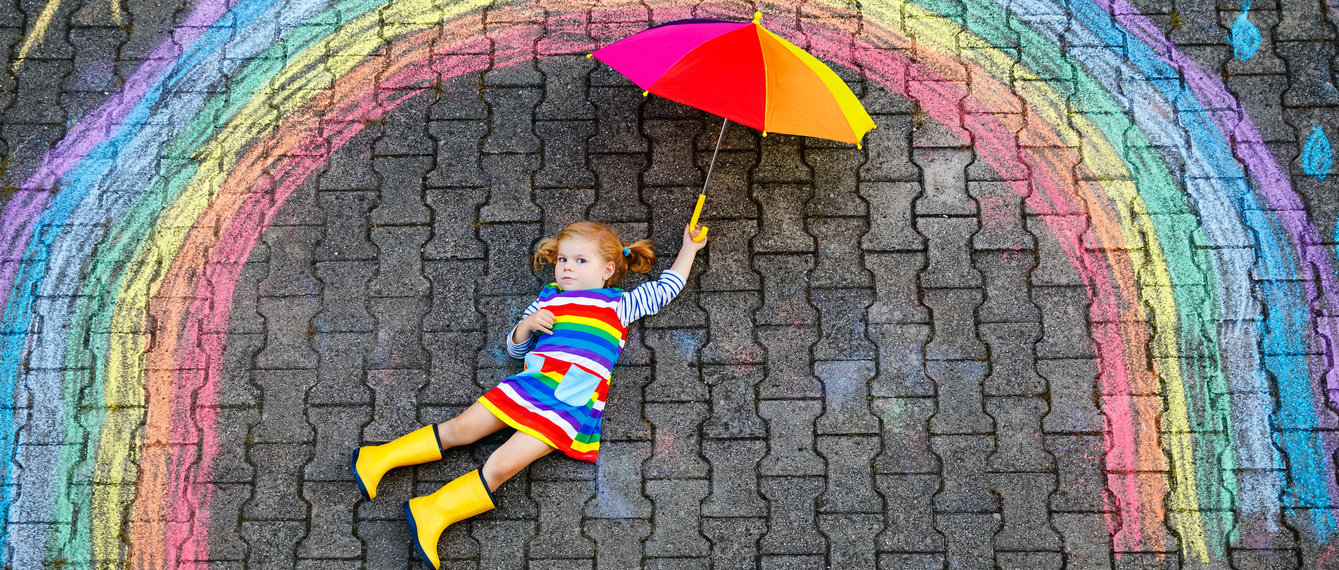 Kind liegt bei selbstgemalten Regenbogen am Boden