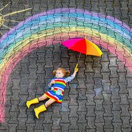 Kind liegt bei selbstgemalten Regenbogen am Boden