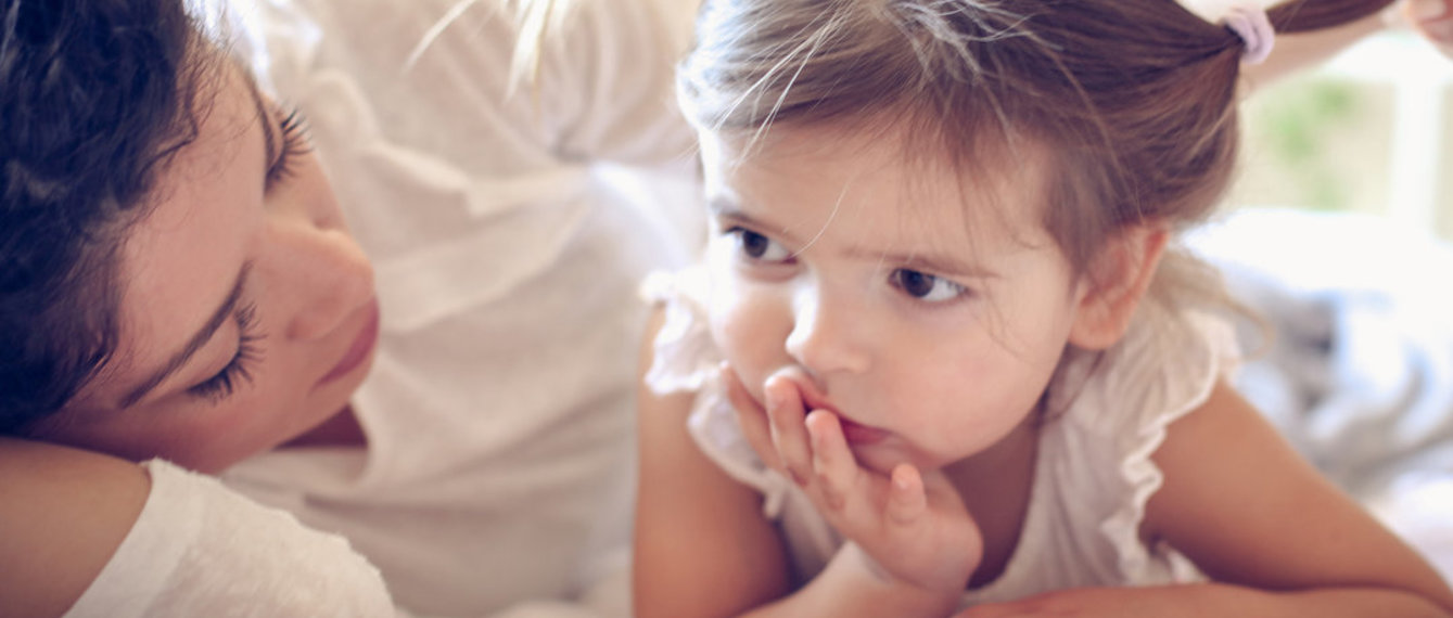 Mama liegt mit Tochter im Bett, Tochter schmollt, Mama tröstet sie