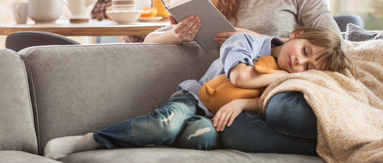 Kind schläft mit Kuscheltier auf Decke und Schoß der Mutter