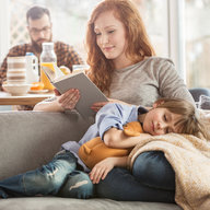 Kind schläft mit Kuscheltier auf Decke und Schoß der Mutter